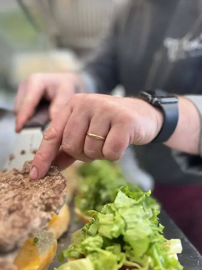 Main déposant un steack sur un burger